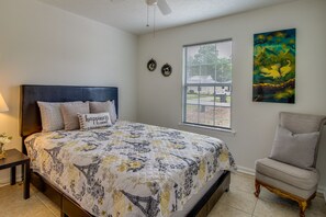 Ein Schlafzimmer mit einem Bett, einem Sessel, einem Fenster und zwei Wandbildern.