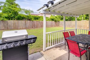 Eine überdachte Terrasse mit Grill, roten Stühlen und einem Tisch.