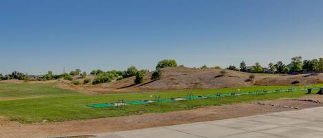 A golf course with a clear sky, a concrete pathway, and green grass.