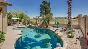 A swimming pool with a curved edge, surrounded by rocks and plants, and a patio area with chairs and a table. - Golfer's Oasis w/ Heated Pool in Avondale! (Avondale)