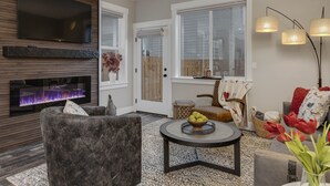 A living room with a fireplace, a flat-screen TV, a sofa, a coffee table, and a lamp. - All New! Maison Monroe in Carlton (Carlton)