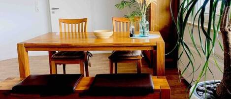 A dining area with a wooden table and chairs, a bench, and a potted plant.