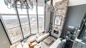 Una sala de estar moderna con chimenea de piedra, ventanas amplias con vistas y una zona de estar acogedora.