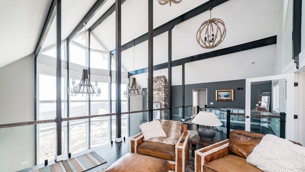 Amplia sala de estar con techo alto, ventanas grandes y vistas a la ciudad. Hay sofás de cuero y una mesa de centro.