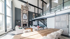 Un salón amplio con una gran mesa de madera, sofás blancos y una chimenea de piedra.