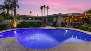 A modern house with a swimming pool, palm trees, and a sunset sky.