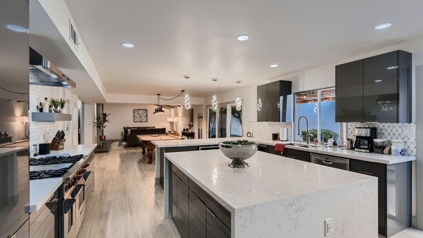 A modern kitchen with a large island, dark cabinetry, and a view to the living area.