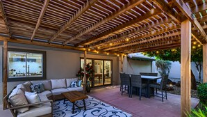 A covered patio with a wooden pergola, a sofa, a table, and a dining set.