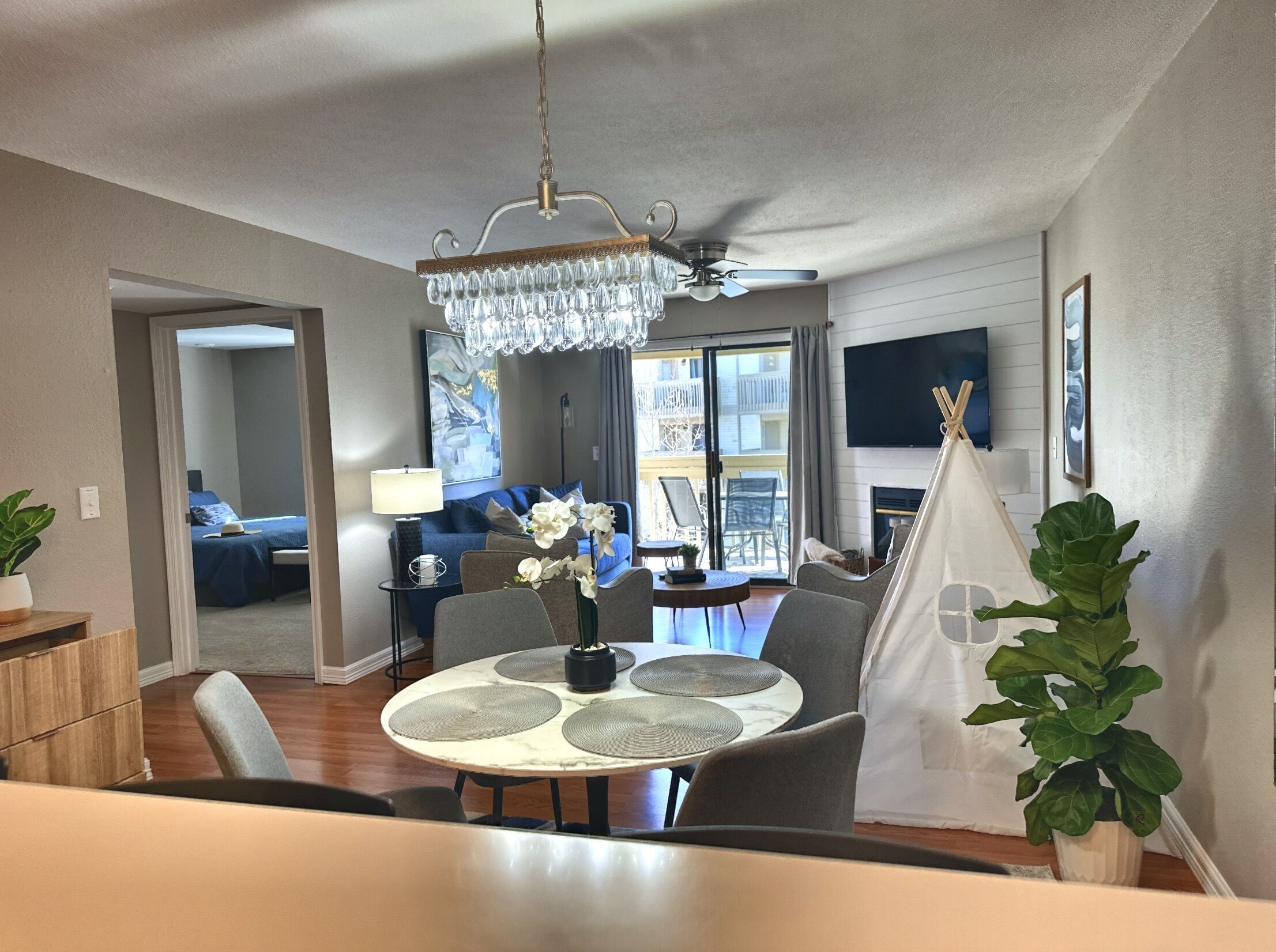 Uma sala de estar moderna com área de jantar, um candelabro, lareira e vista para a varanda.
