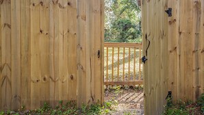 Una verja de madera con un cerrojo metálico, que da acceso a una terraza de madera.