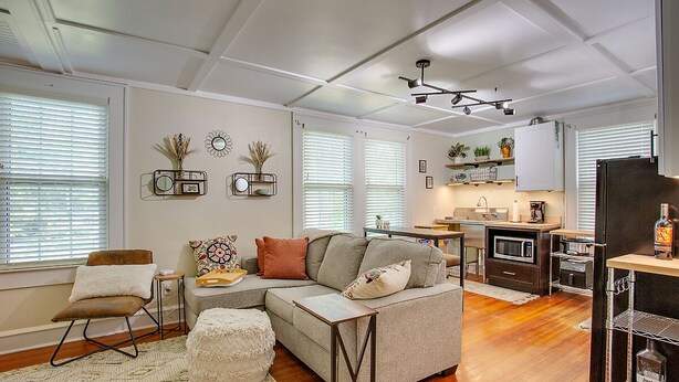 Una sala de estar moderna con un sofá seccional, una pequeña mesa de comedor y una zona de cocina con microondas y refrigerador.