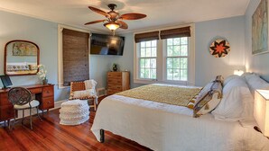 Un dormitorio con cama, escritorio, silla, ventilador de techo y televisor.