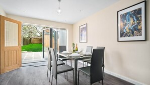 A dining area with a table set for four, a wooden door, and a view of a garden through glass doors.