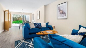A modern living room with a blue sofa set, a wooden coffee table, and a framed abstract painting on the wall.