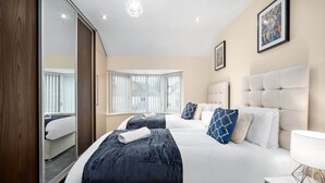 A hotel room with a large bed, a mirror, a window with blinds, and a painting on the wall.