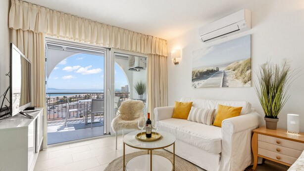 A modern living room with a white sofa, a round coffee table, and a view of the beach through a glass door. - WELCS ESTUDIO 057 EMP Frente al Mar (Empuriabrava)