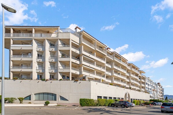 A multi-story hotel with balconies, a parking area, and a clear sky. - WELCS APARTAMENTO 216 EMP Frente con Terraza (Empuriabrava)