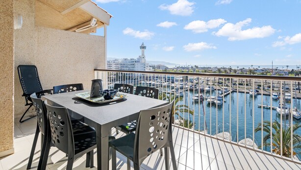 A balcony with a table and chairs overlooking a marina with boats and a distant tower. - WELCS APARTAMENTO 216 EMP Frente con Terraza (Empuriabrava)