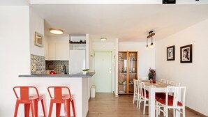 A modern kitchen with a bar area, white dining chairs, and a wooden dining table. - WELCS APARTAMENTO 216 EMP Frente con Terraza (Empuriabrava)