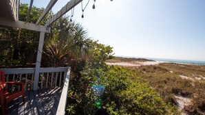 Eine Holzterrasse mit einem roten Stuhl, Blick auf einen Strand mit Dünen und dem Meer.