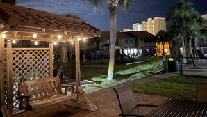 A gazebo with string lights, a palm tree, and a patio area with a bench and table. - Pool in Backyard and steps to beach (Panama City)