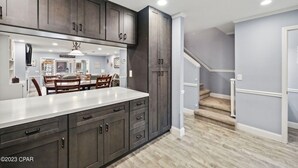 A modern kitchen with dark cabinetry, a white countertop, and a dining area with wooden chairs. - Pool in Backyard and steps to beach (Panama City)