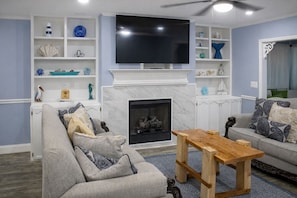 A living room with a fireplace, a television mounted above it, and a sofa with decorative pillows.