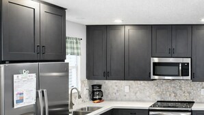 A modern kitchen with dark cabinets, stainless steel appliances, a microwave, and a coffee maker. - Pool in Backyard and steps to beach (Panama City)