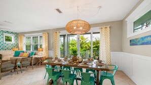 A dining area with a large table set for six, surrounded by green chairs, and a hanging rattan light fixture above.