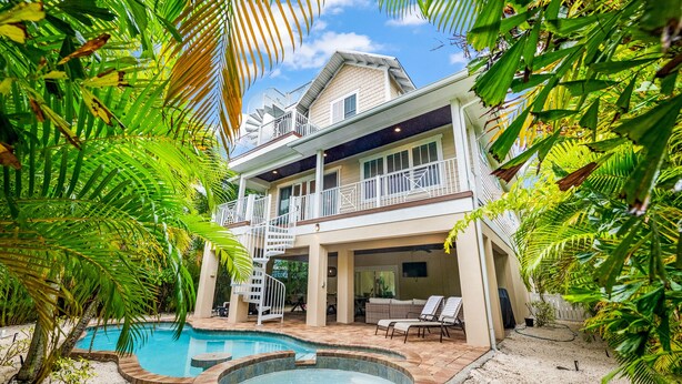 A two-story house with a swimming pool and hot tub, surrounded by lush greenery.