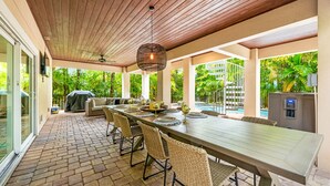An outdoor dining area with a long table, wicker chairs, and a hanging light fixture.