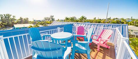 Una terraza con sillas Adirondack azules y rosadas, una mesa redonda y una barandilla blanca.