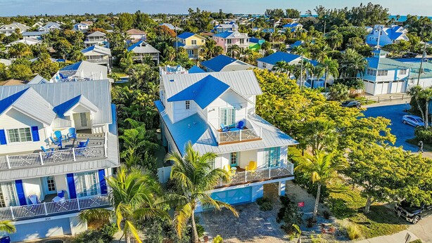 A coastal residential area with houses featuring blue roofs and white walls, surrounded by lush greenery and palm trees.