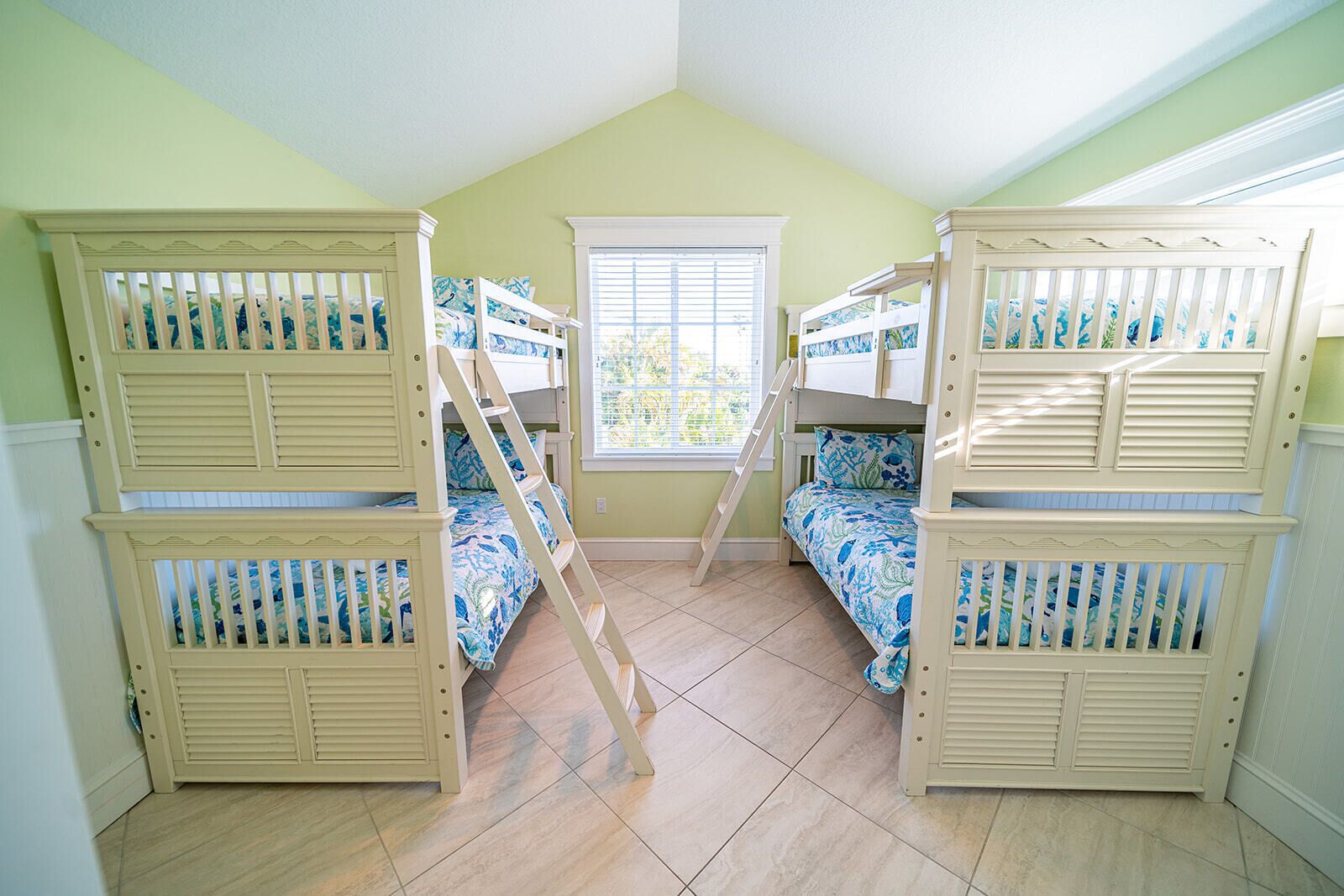 A room with two bunk beds, a window with blinds, and a light green wall.