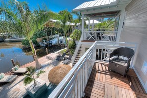 A balcony with a view of a pool and palm trees, a wicker chair, and a small table. - Canal-Front Oasis with Private Dock, Pool, Near Beach and Shops - Aqua Cove (Anna Maria)