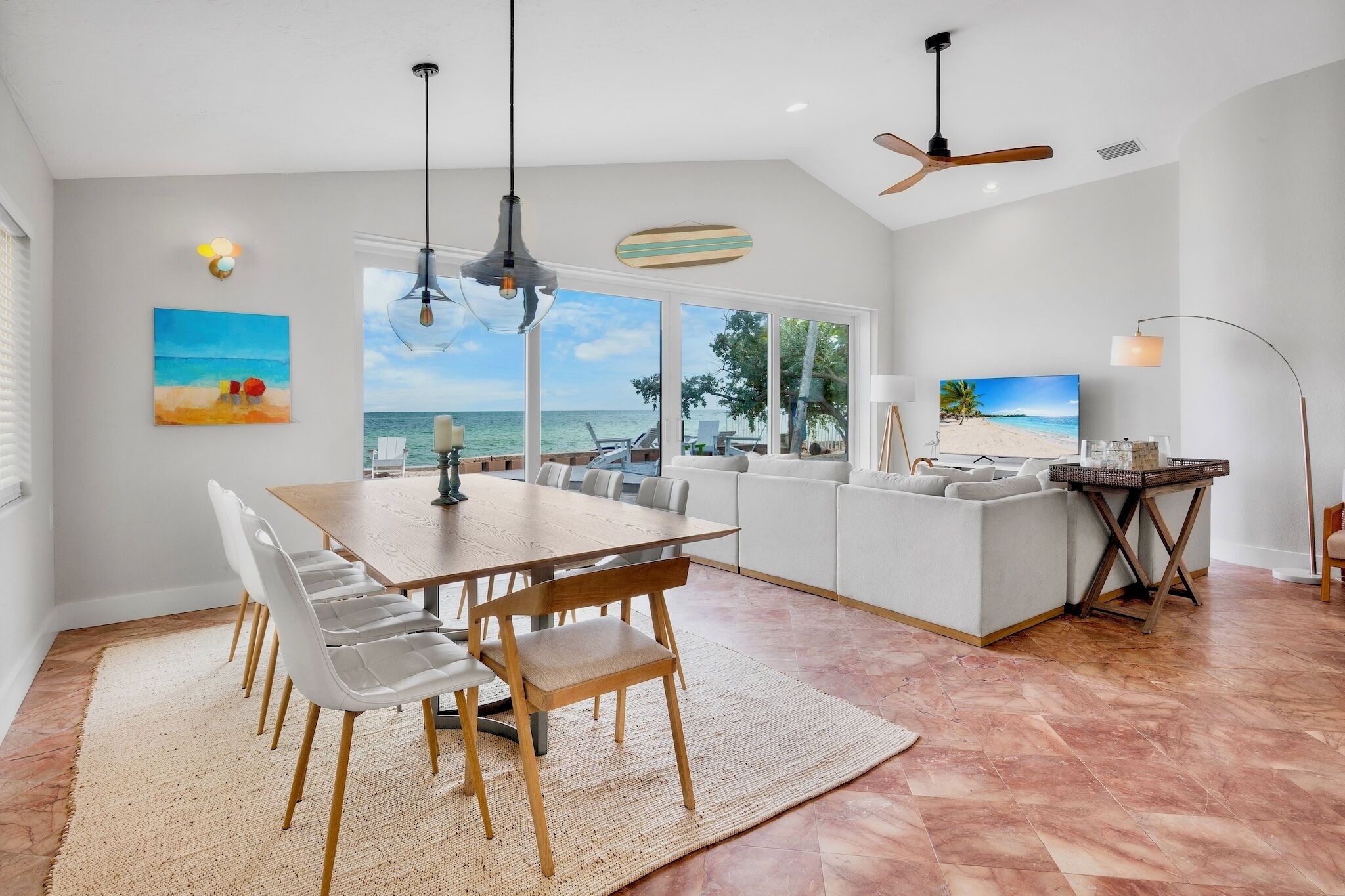 Una sala de estar moderna con comedor, ventanas amplias con vista al mar y un ventilador de techo.