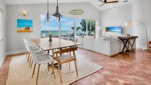 A modern living room with a dining area, large windows with a view of the sea, and a ceiling fan. - Bayfront Home with Amazing Water Views! Private pool! – Breakaway (Anna Maria)
