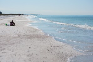 A beach with a person sitting on the sand, a green bucket, and a blue bucket. - Beach Front Home with Direct Access to Beach and Beautiful Sunset Views (Anna Maria)