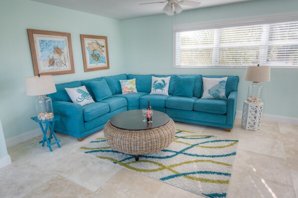 A teal-colored sectional sofa with decorative pillows, a round wicker coffee table, and a patterned rug.
