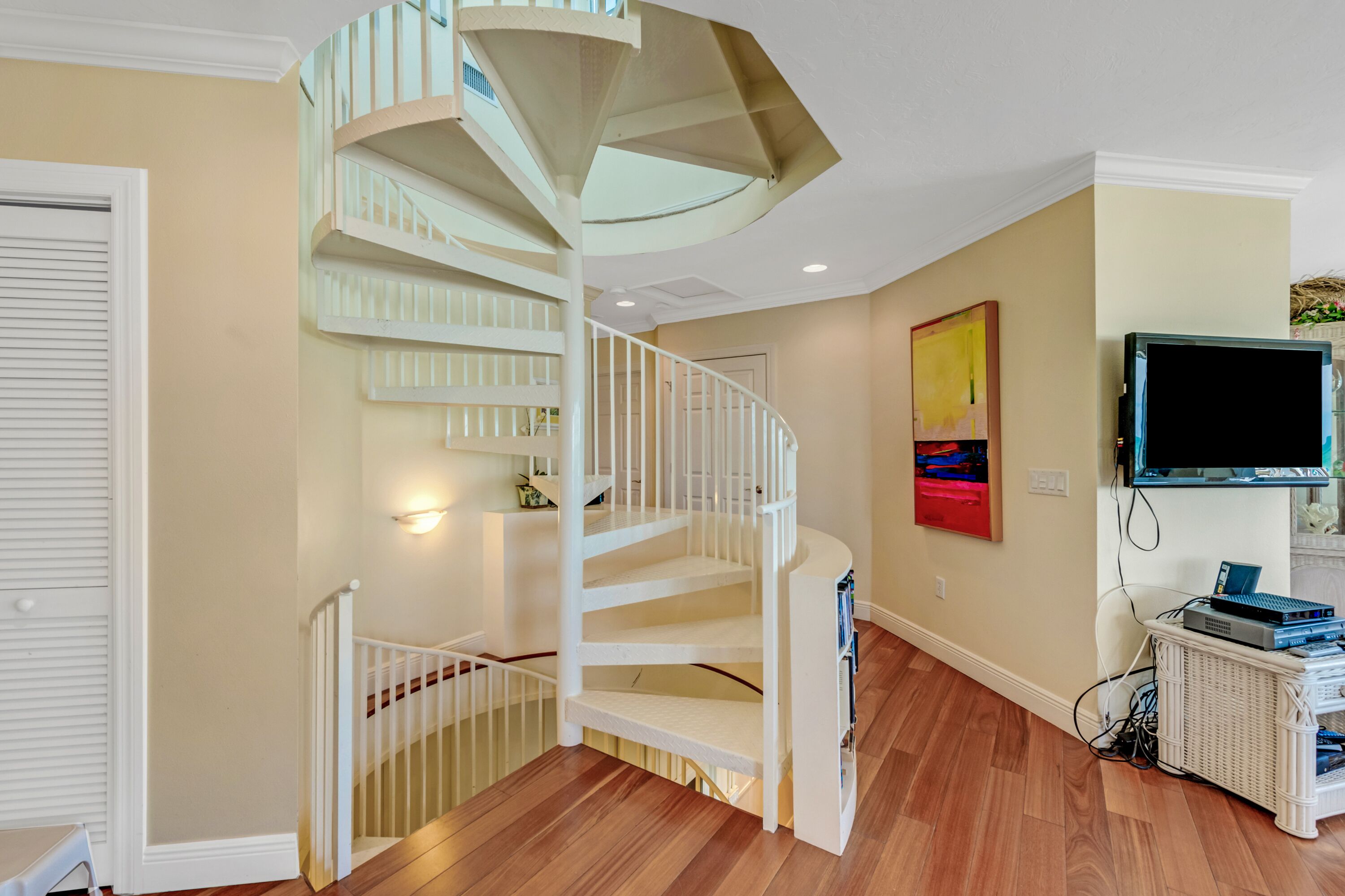 A modern interior with a spiral staircase, a flat-screen TV, and a wicker side table.