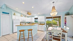 A modern kitchen with white cabinets, a central island with stools, and a dining area with a table and chairs. - Canal Front Home with Dock, Saltwater Pool, Ping Pong - Ama Maria (Anna Maria)
