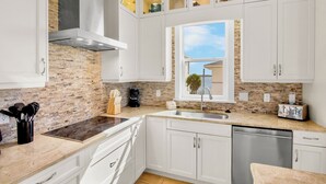 Une cuisine moderne avec des meubles blancs, un mur de fond en briques, une cuisinière encastrée et une fenêtre offrant une belle vue.