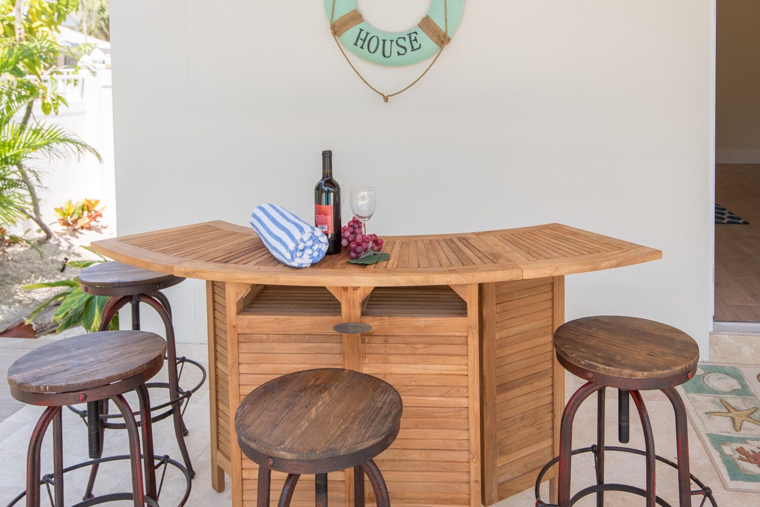 Un comptoir en bois avec des tabourets, une bouteille de vin et un verre posés dessus.