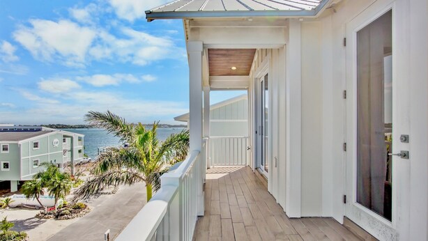 Un balcon avec vue sur l’océan, une terrasse en bois et un bâtiment à la façade blanche.