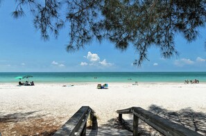 A beach with wooden benches and a clear view of the ocean. - Private Pool, Ping Pong and Foosball! Views of the Bay! (Bradenton Beach)