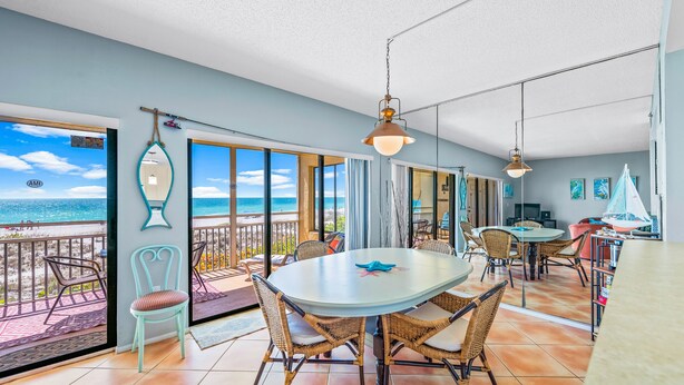 Un vaste espace dédié à la salle à manger, avec une grande table ronde et des chaises en osier, donnant sur un balcon d’où l’on peut admirer la plage et l’océan.