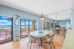 A spacious dining area with a large round table and wicker chairs, overlooking a balcony with a view of the beach and ocean. - AMI Escape! Direct Beach Access, Gulf Views and Walk to Holmes Beach Shops (Holmes Beach)