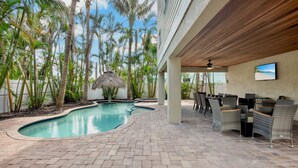 A pool area with a curved design, surrounded by palm trees and a covered seating area with wicker furniture.