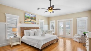 A bedroom with a large bed, a ceiling fan, and a painting on the wall.