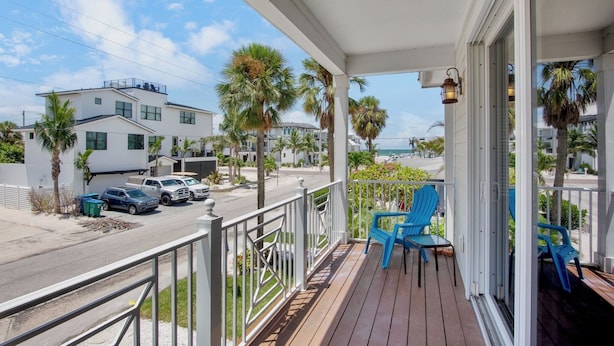 A wooden deck with blue chairs, a railing, and a view of the street and beach.